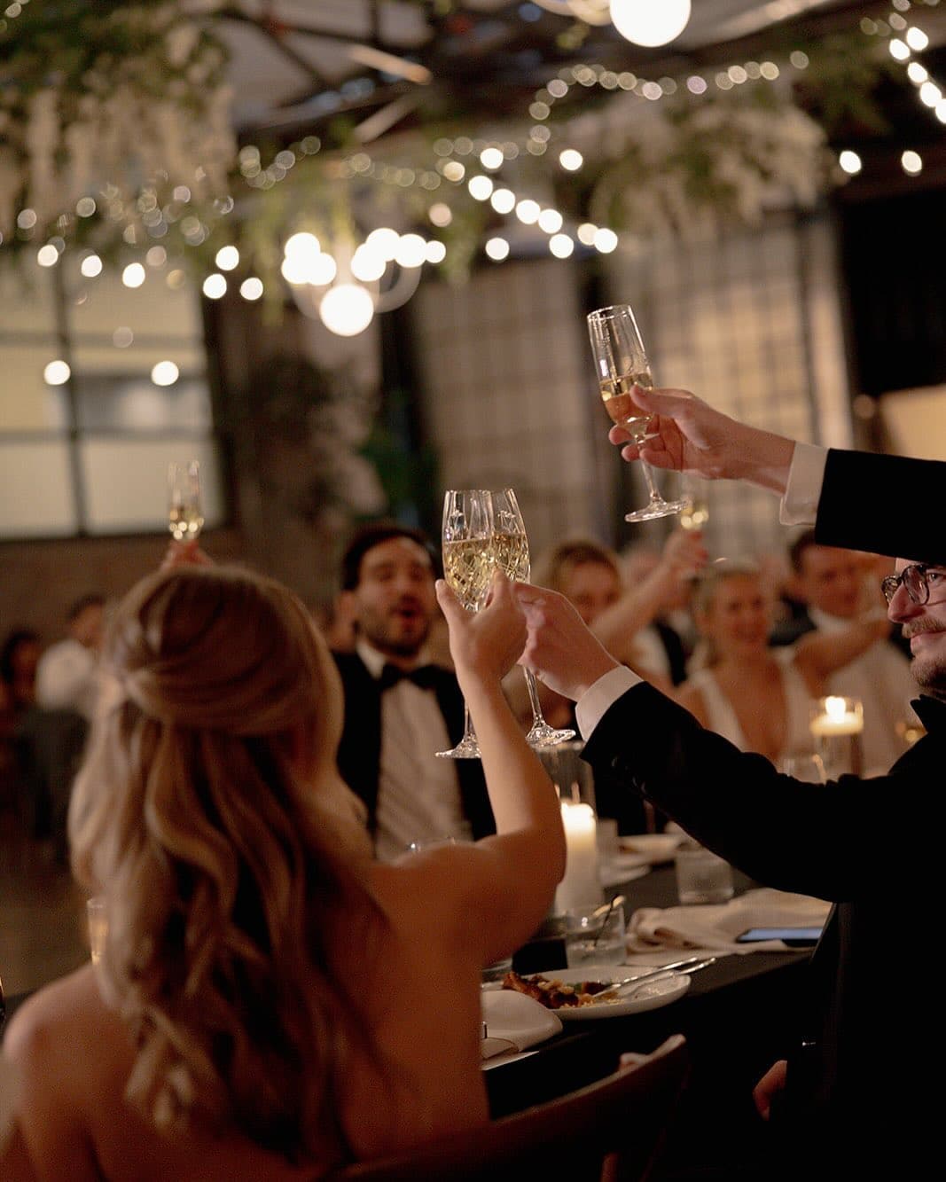 Champagne toast under string lights at reception