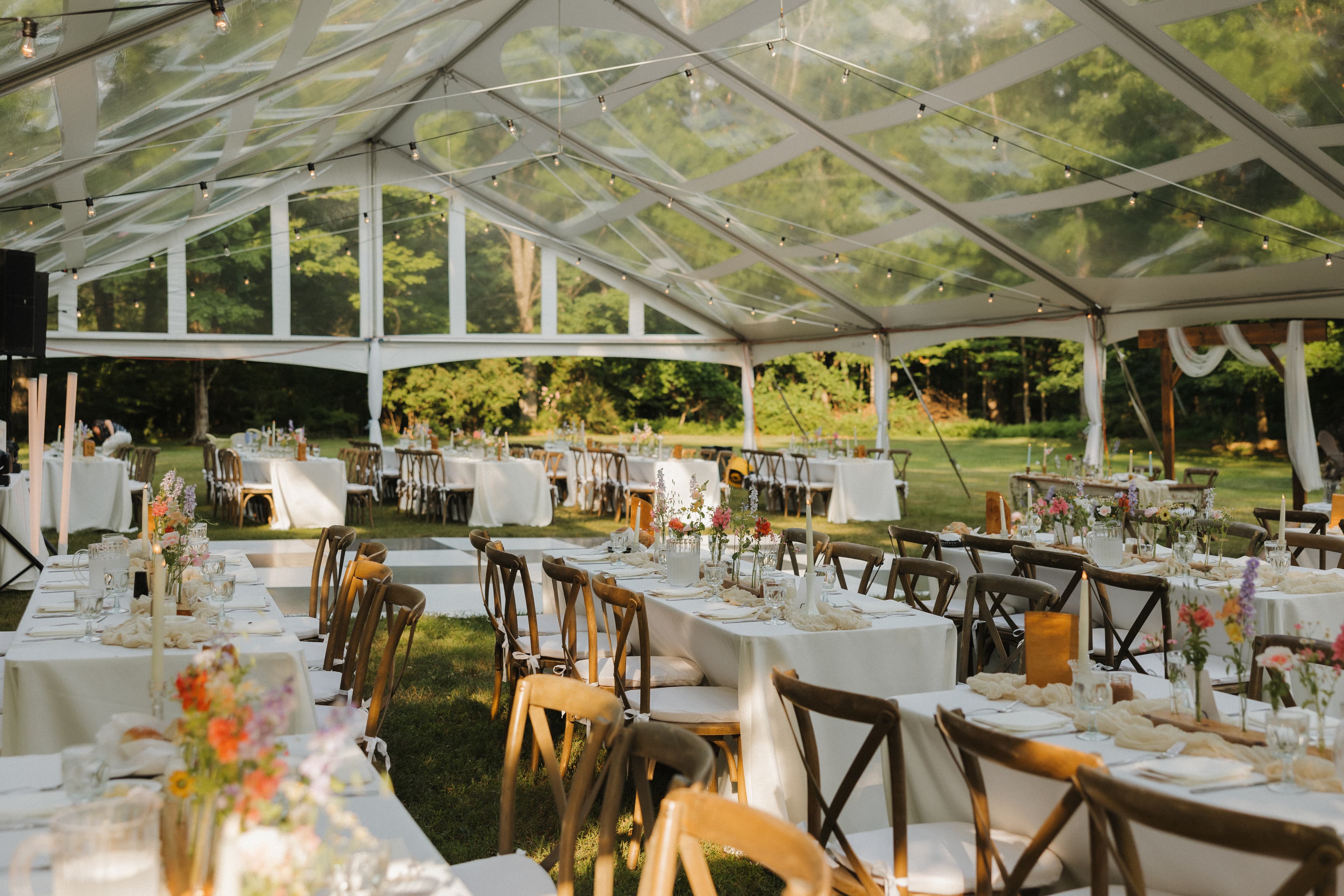 Tented reception with crossback chairs, wildflower centerpieces, and string lights