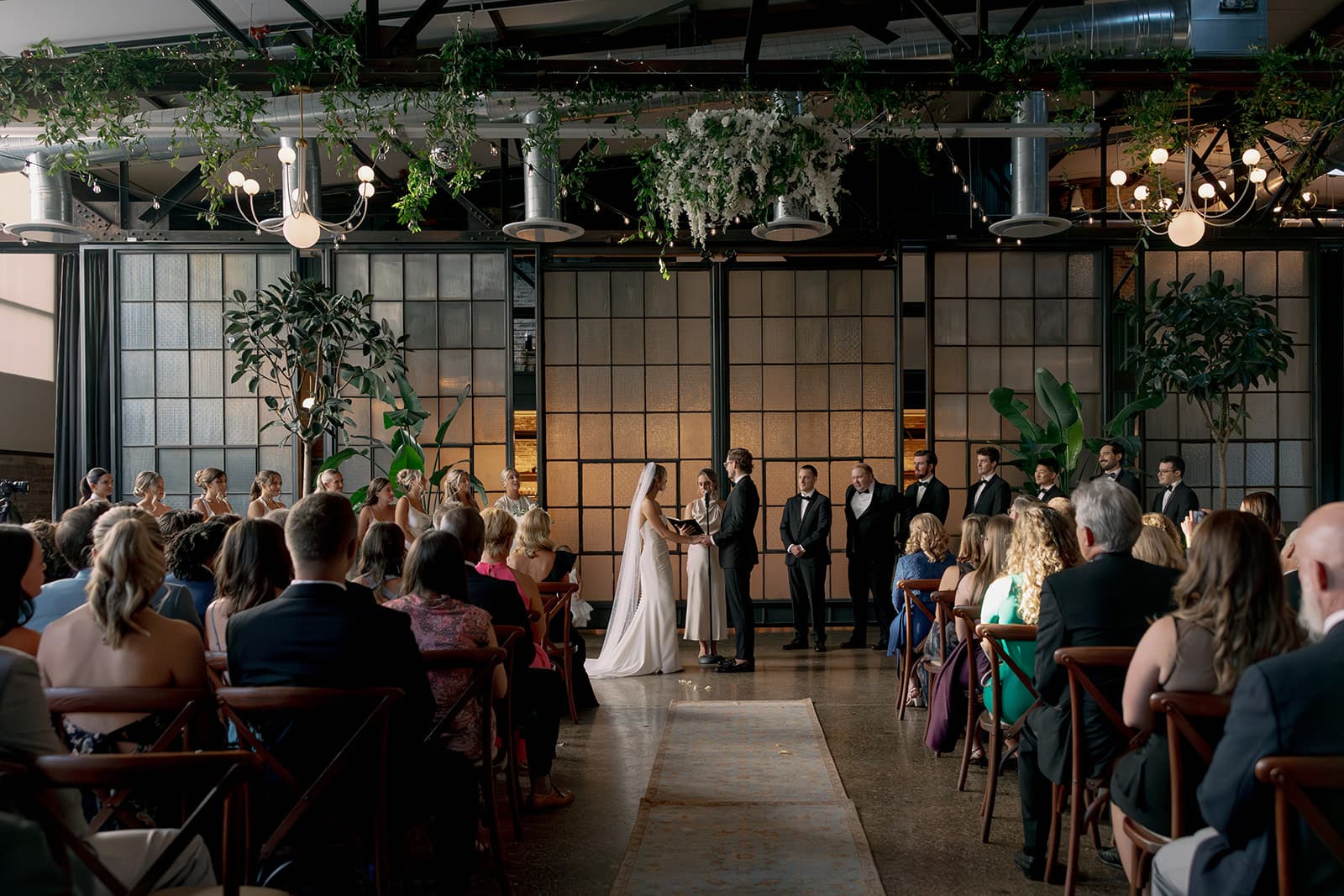 Industrial venue ceremony with hanging greenery and chandeliers