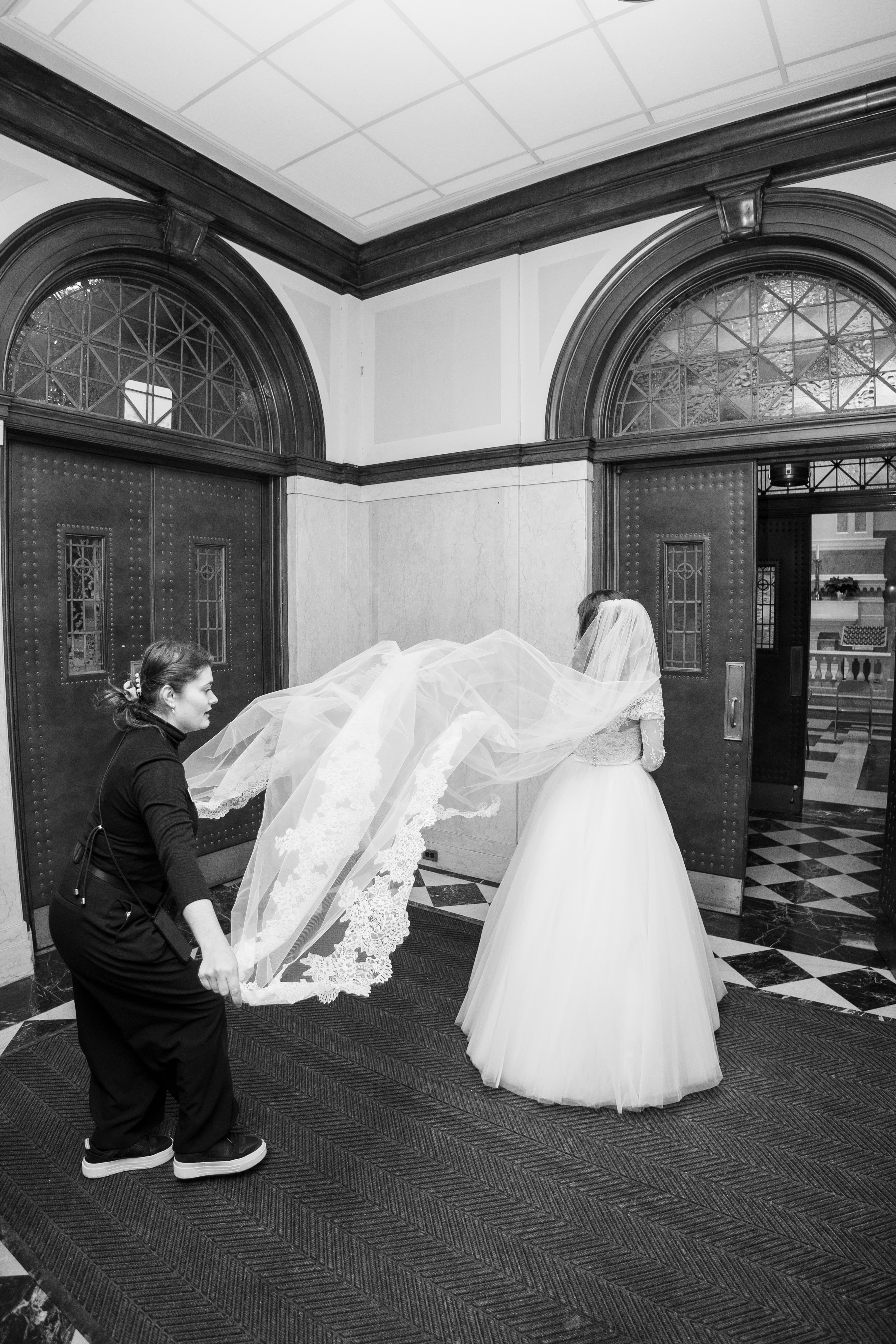 Coordinator adjusting bride's cathedral veil before ceremony