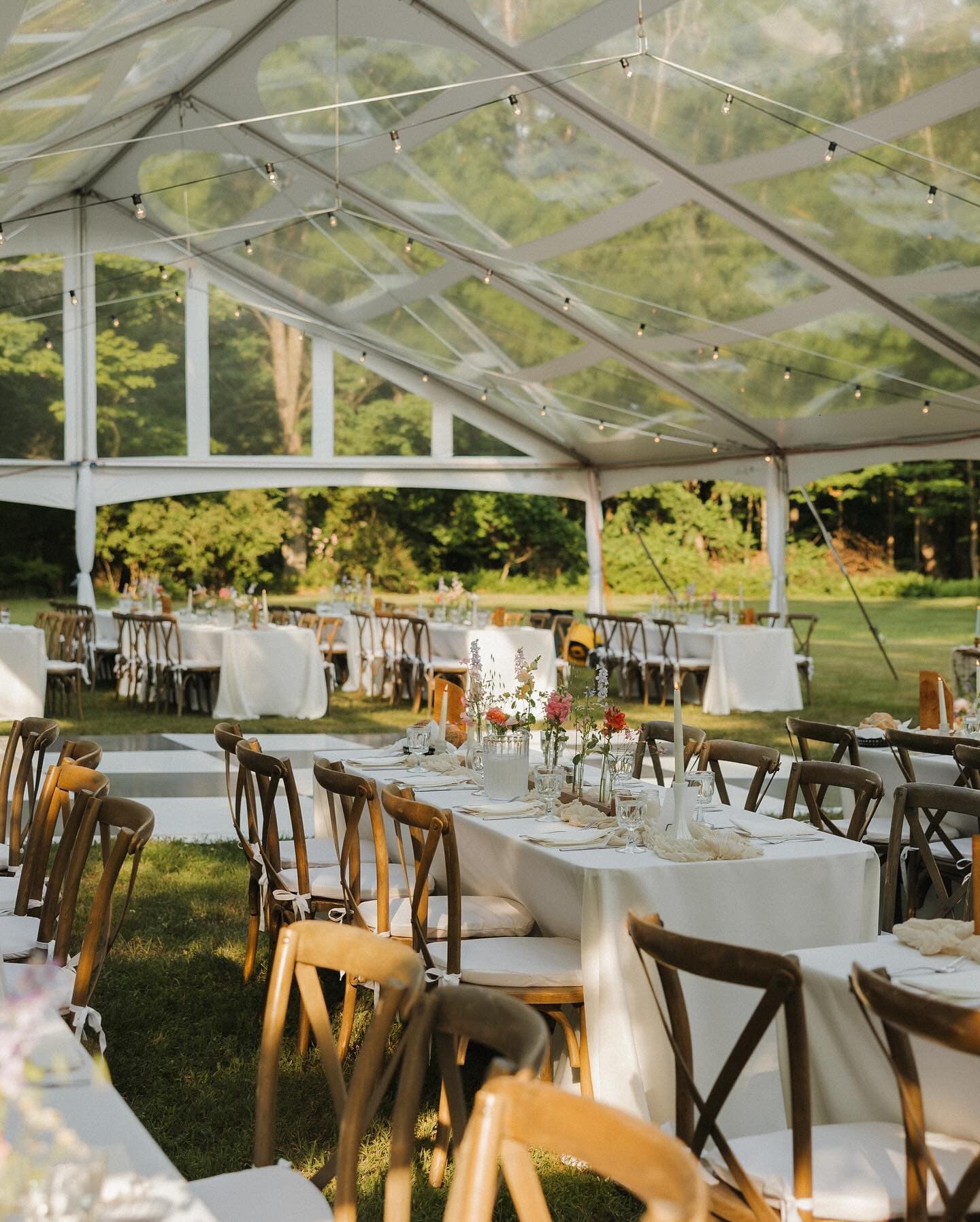Clear tent reception with crossback chairs and string lights